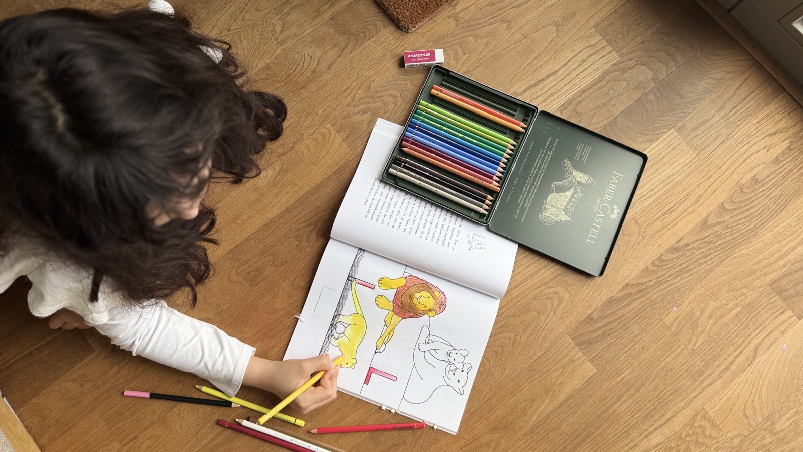 A child coloring a book beside a box of colored pencils